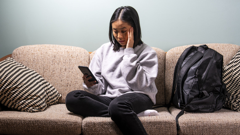 A college-age woman looking stressed at her phone