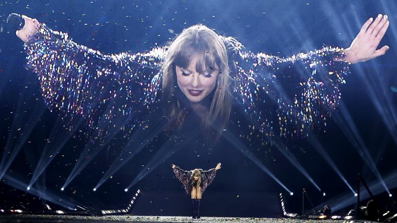 Taylor Swift taking a deep bow during the Eras Tour, in front of a massive video image of the same