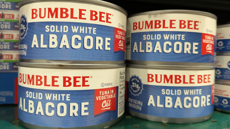 A shelf stacked full of Bumble Bee Solid White Albacore tuna, with four cans in prominent foreground.