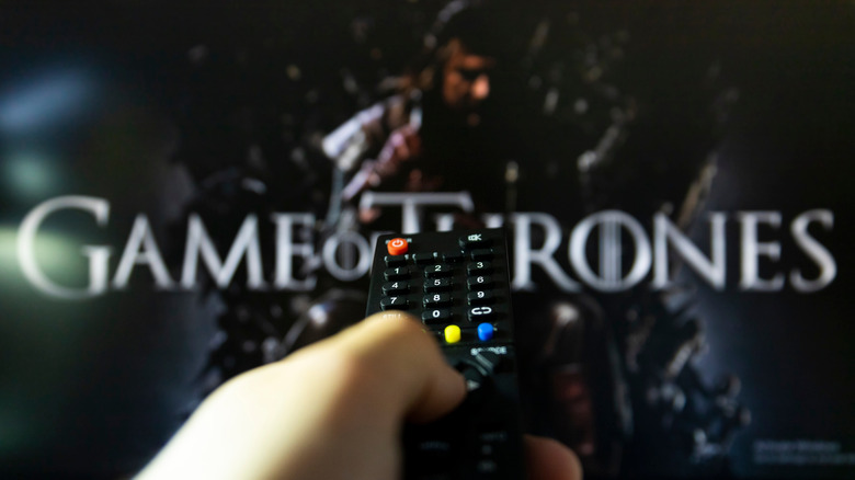 Hand holds TV remote and points it at screen with Game of Thrones text