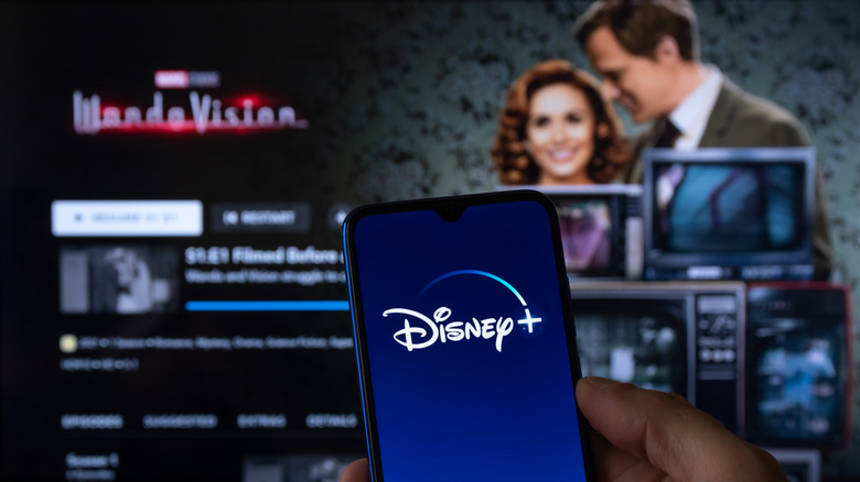 Close up of smartphone with Disney+ logo while WandaVision series appears on TV screen in background