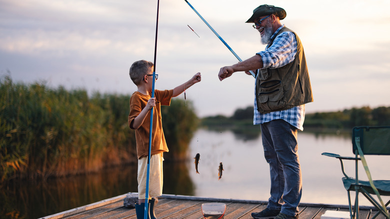 A granddad fishing with his grandson on a wooden dock by a lake or river.