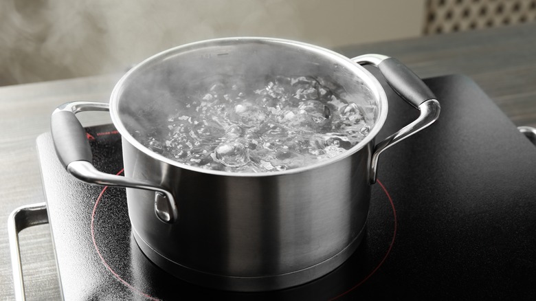 Cooking pot with boiling water and stove on wooden table against grey background.