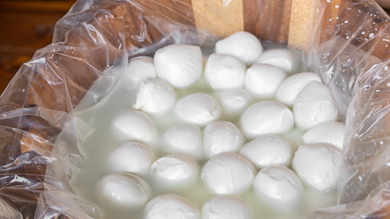 Small mozzarella balls soaking in brine inside a plastic bag in wooden bowl.
