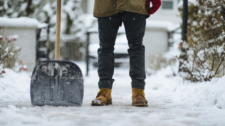 Shovel and boots of a man after cleaning path from snow in driveway.