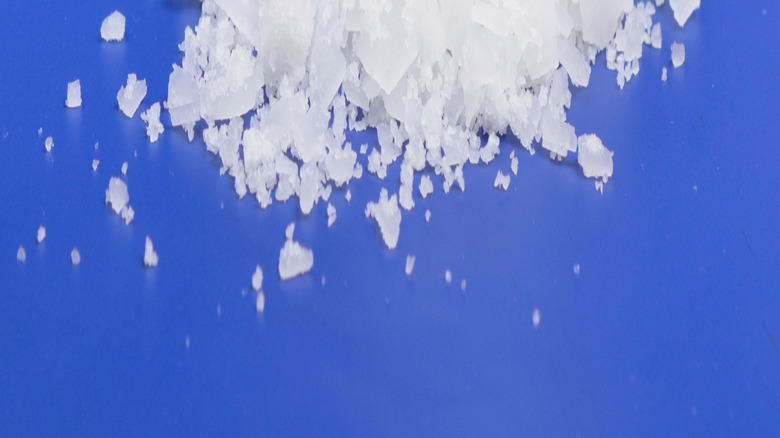 A pile of magnesium chloride against a blue background with a bottle behind it.