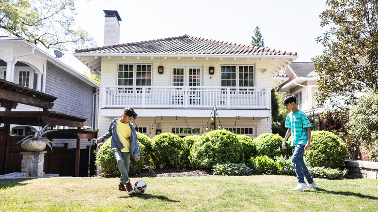 Two young boys playing soccer in a landscaped backyard behind a beautiful white house.