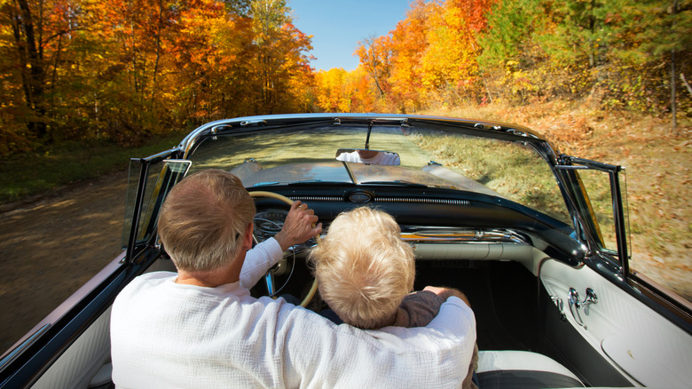 A rearview of an elderly couple in a car driving on a backroad