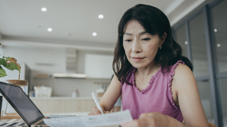 A woman is at home, holding a collection of paper bills and financial plans.