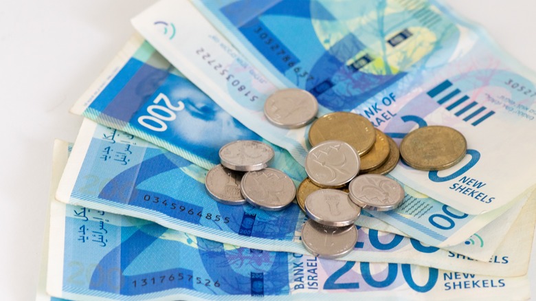 Close-up of Israeli new shekel banknotes, with coins scattered on top.
