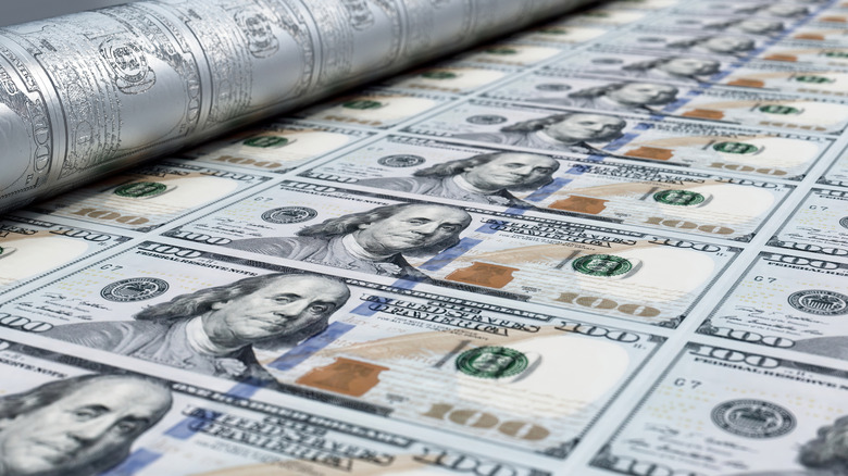 A close-up illustration of a printing press, as new hundred dollar bills are being printed and rolled out on a conveyor belt.