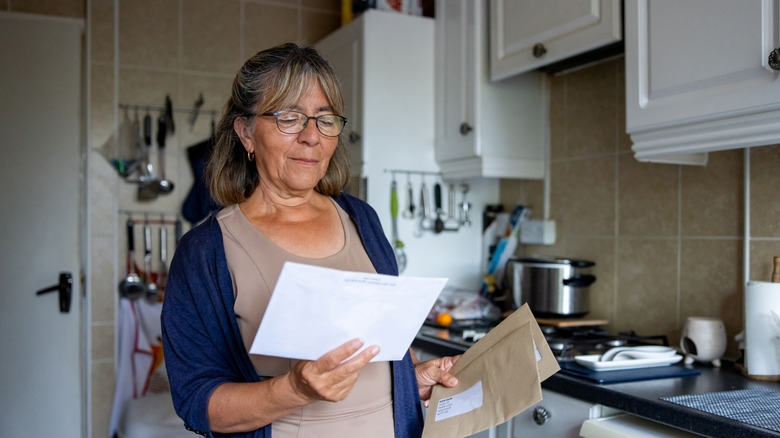 An older woman looking at her mail in the kitchen