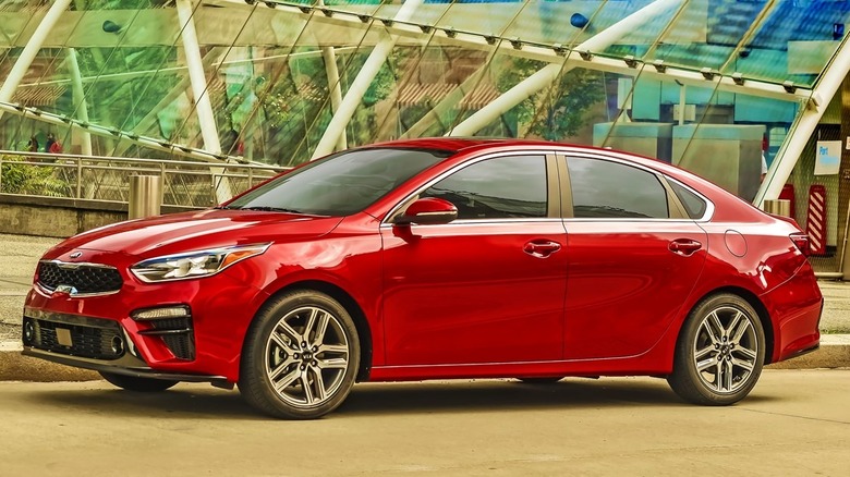 A red Kia Forte parked near a glass structure outside.