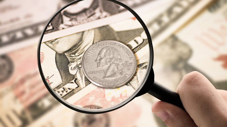 A U.S. quarter under a magnifying glass on top of a stack of $10 bills
