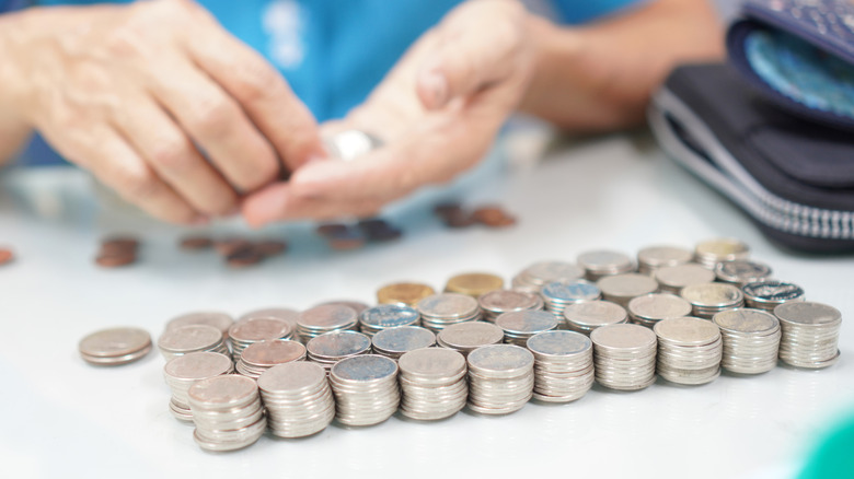 A person counting many coins in stacked rows by hand