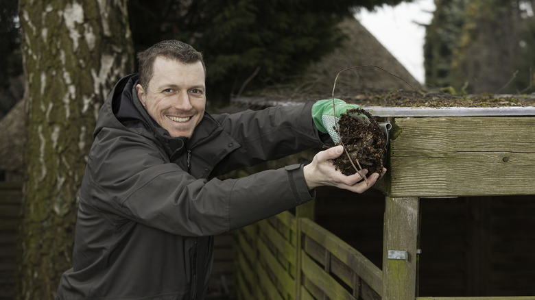 A smiling man cleaning the gutters on his home.