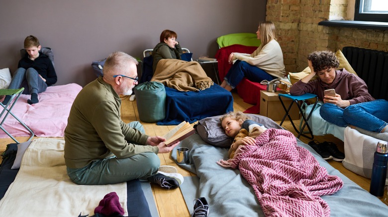 A family in a shelter sitting and laying down on cots