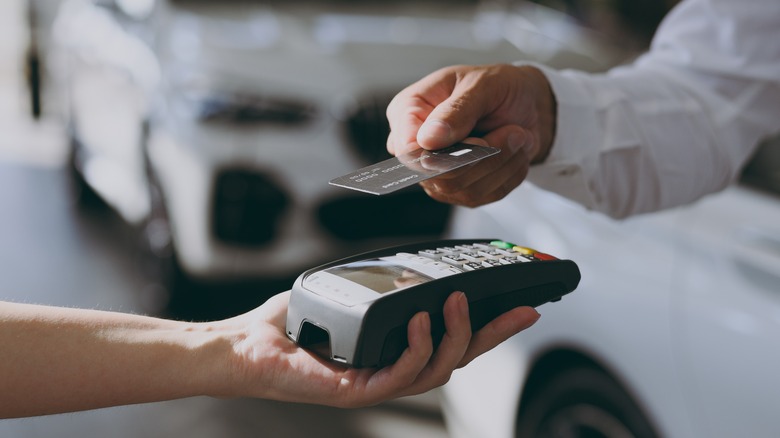 A man holding a debit card over a card reader in a car dealership
