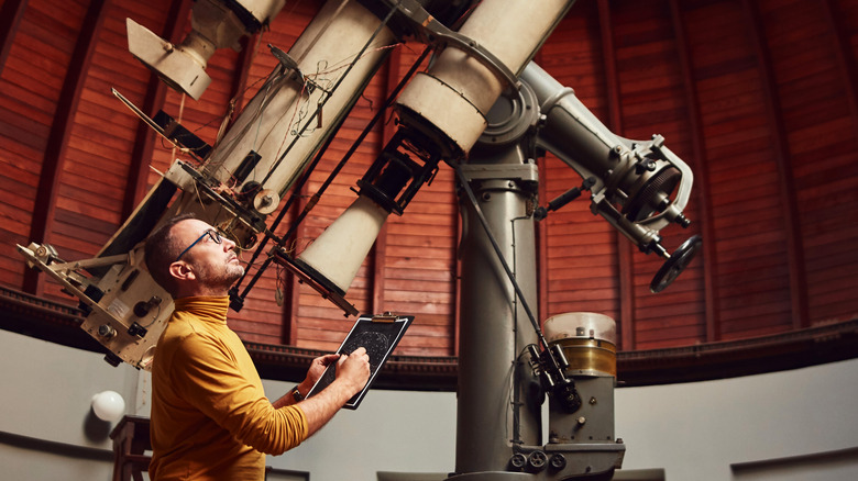 Picture of man by large telescope who is looking up and sketching on a clipboard.