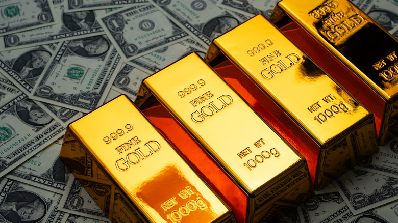 solid gold bars placed on scattered one dollar bills