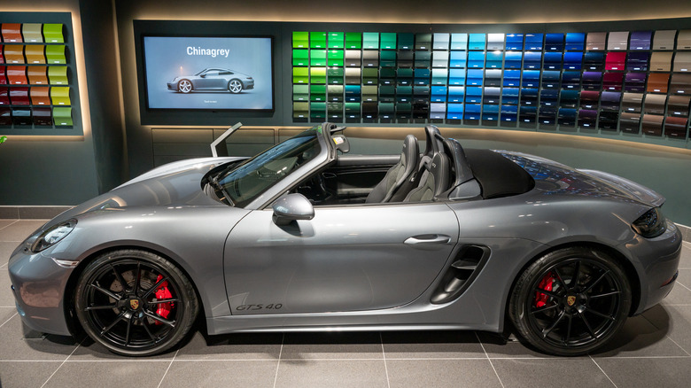 Gray Porsche 718 Boxster GTS 4.0 convertible displayed in a showroom with paint color samples on the wall behind it
