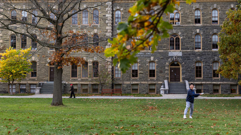 An exterior view of Cornell University with a student tossing a frisbee