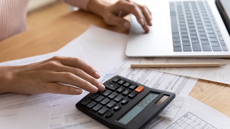 Person calculating with calculator, laptop