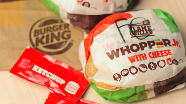 A pair of wrapped Whopper Juniors with cheese on a laminate table.