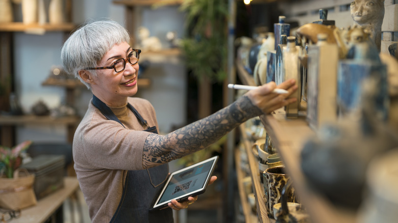 Senior woman observing pottery studio with tablet in hand