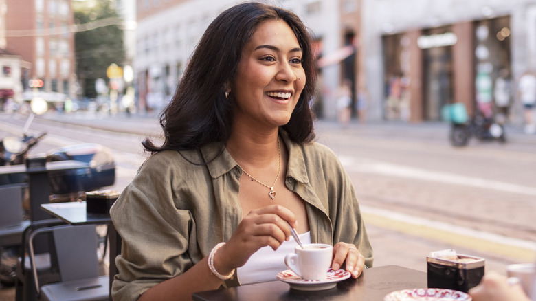 smiling young woman stirs her coffee on an Italian café's patio
