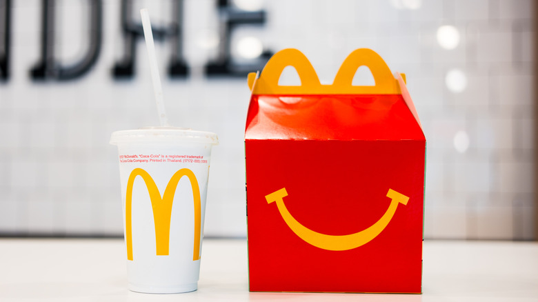 Red plastic McDonald's Happy Meal box with cartoon eyes and a yellow arches handle on a plain white background