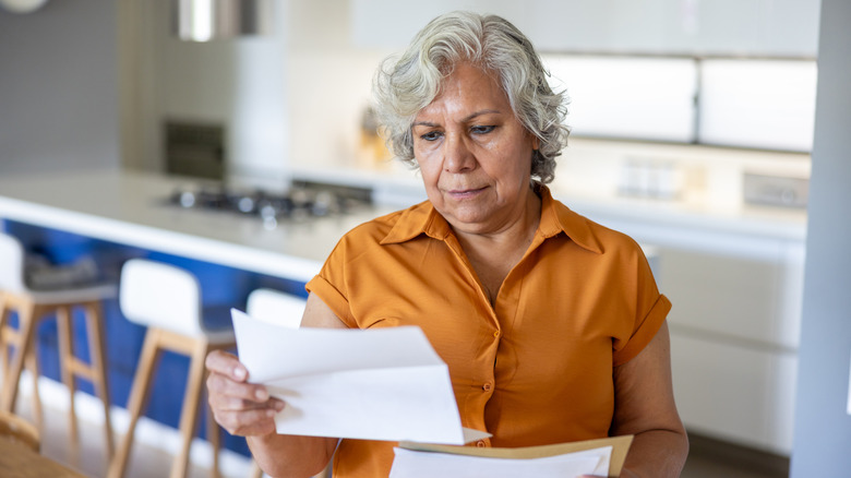 Woman looking at paperwork in kitchen.
