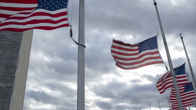 United States flags flown at half mast under gray skies.