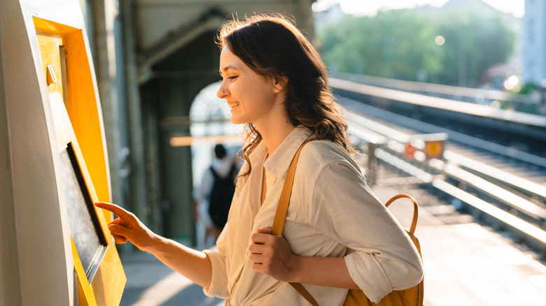 Young woman buying a train ticket at kiosk