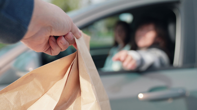 Person handing bag to customer in car drive through line