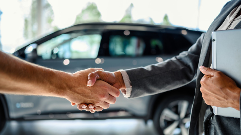 A buyer of the car shaking hands with the seller in the auto dealership