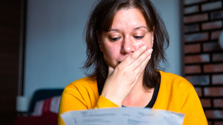 Woman in yellow sweater upset looking at bill