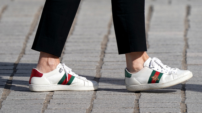 A close-up of man wearing Gucci Ace sneakers while walking in the street.
