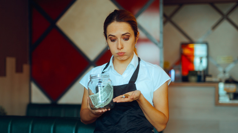 A server looking disappointed as she holds a tip jar