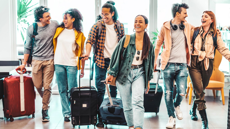 A group of happy young adults wheeling luggage trolleys