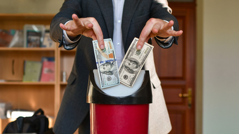 Person throwing $100 bills into a trash can