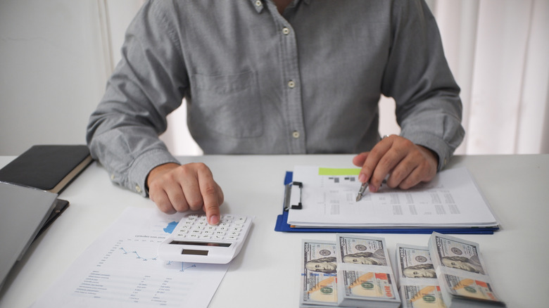 Person sitting with paperwork and money on table.