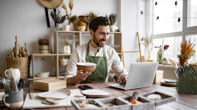 A ceramic shop owner using a laptop while working in a store.