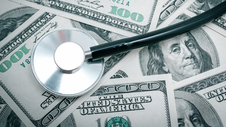 Round portion of stethoscope sits on top of scattered $100 bills