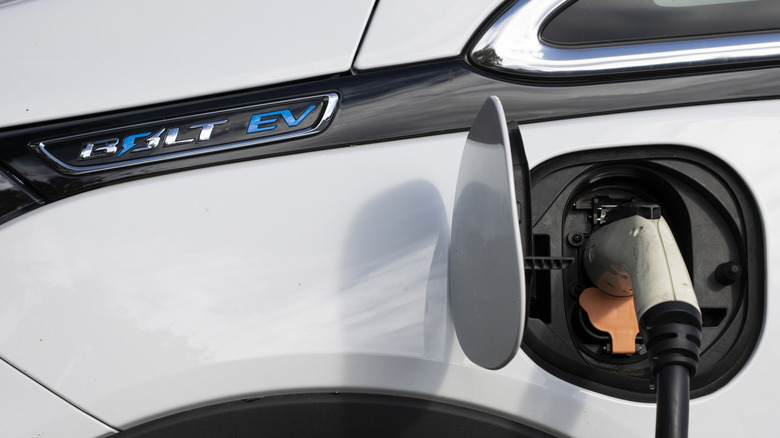 Closeup of a Chevy Bolt EV electric car charging at a public charging station in a parking lot.