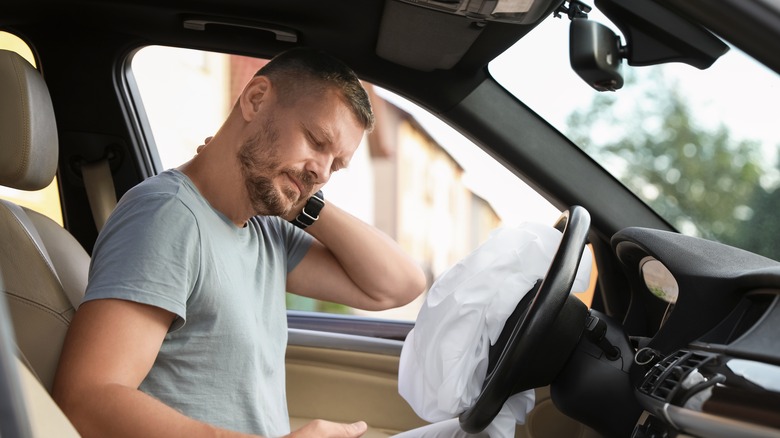 A man injured in a car accident holding his neck in front of a deployed airbag.