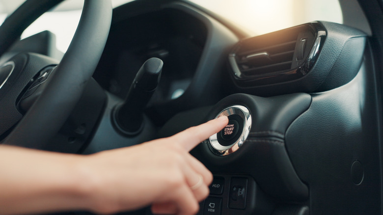 A hand pressing an ignition button in a vehicle.