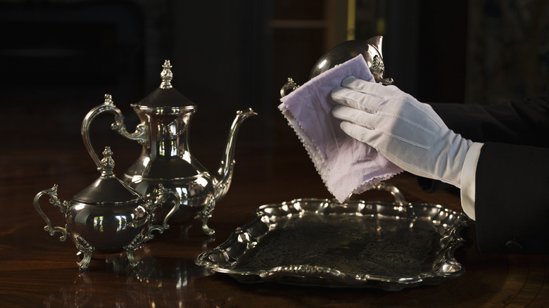 a butler polishes silverware with gloved hand