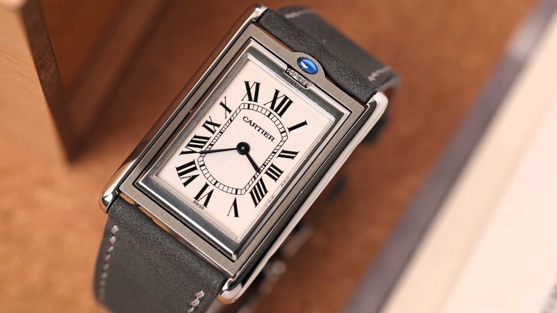 Close-up of a rectangular Cartier Tank watch with a white Roman-numeral dial, blue hands and crown, and dark gray leather strap
