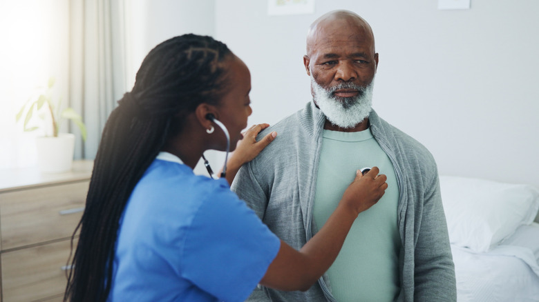 A young doctor listens to an older male patient's heartbeat through a stethoscope